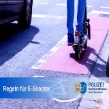 Fahrbahn mit rotem Streifen als Radweg auf dem ein E-Scooter mit Beinen einer Person zu sehen sind